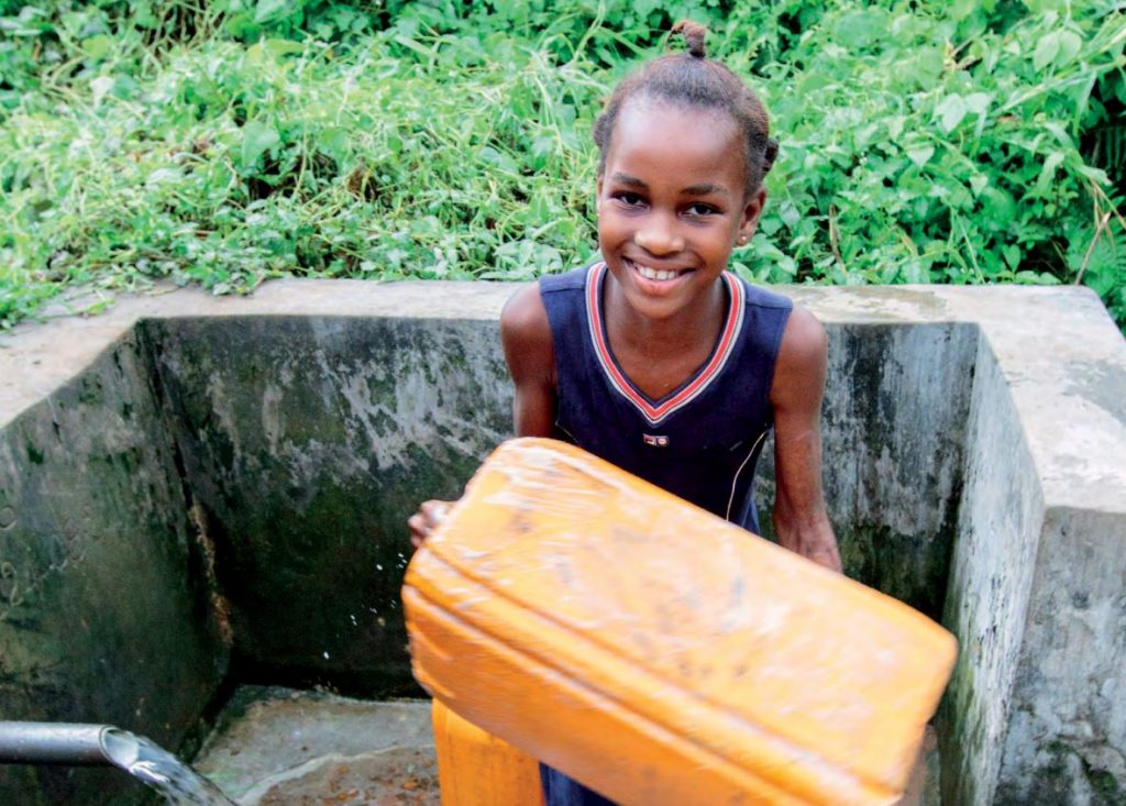 Smiling young women holding an orange water jug close to an outdoor water tap