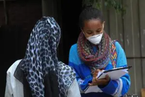 2 women in discussion: one from the back with a head scarf, the other facing her with a face mask, h