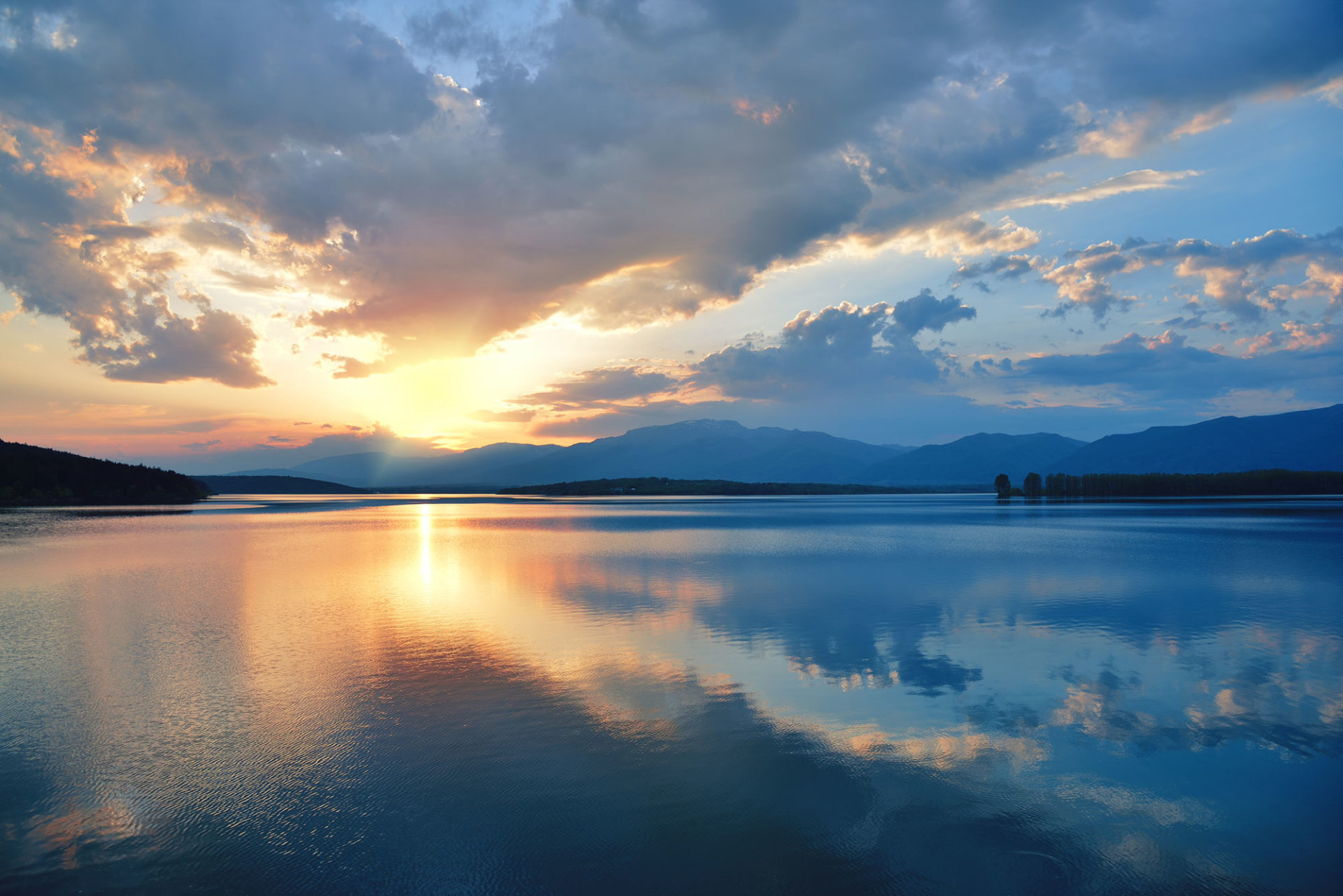 Sun rise over a large body of still water with clouds reflecting the orange sunlight