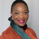 Woman in orange shirt with bright blue braids and pink lipstick with a broad smile