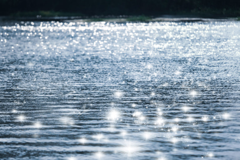 Blurry water wave ripple with bright abstract bokeh of sun ligh.Nature background.