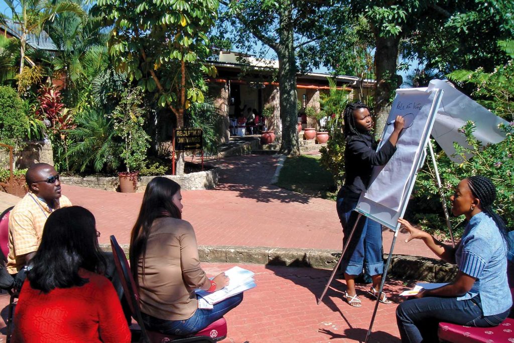 A person presenting something on a flip chart, 3 people looking at her facing back to the camera