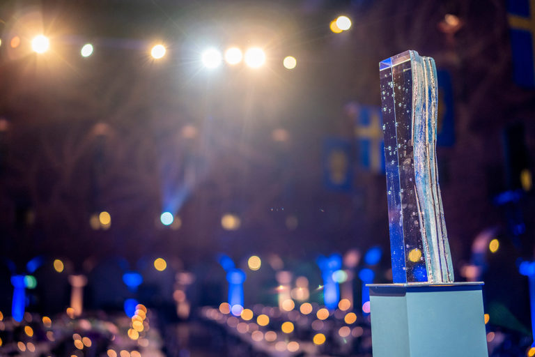 Stockholm Water Prize statue in front of the Stockholm City hall banquet room, with blue and yellow lights creating an artistic blur effect in the background