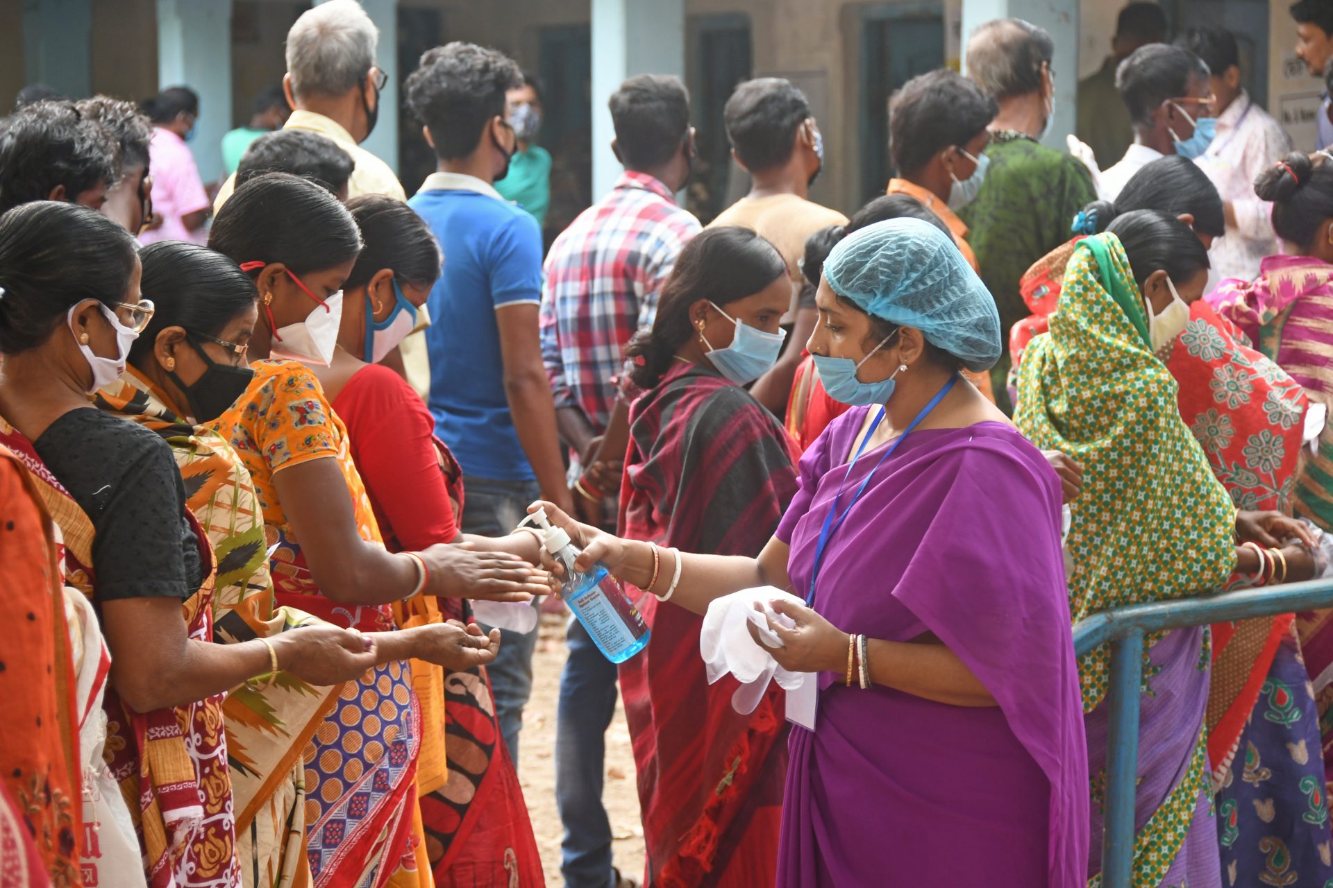 Group of women in sarees waiting for their turn to get hand sanitizers. All people are covered in facemasks.