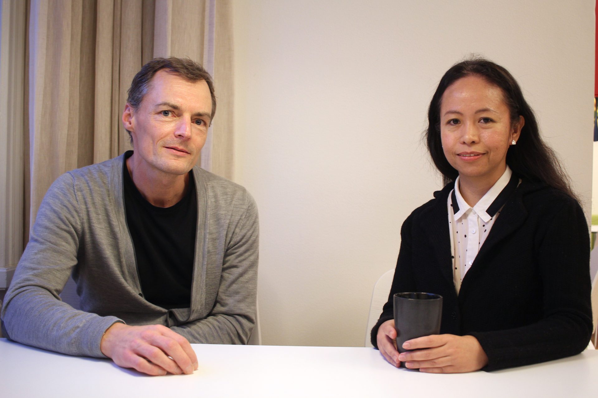 Nicolai and Iris with a coffee mug sitting at a table, looking at the camera