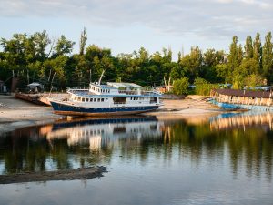 Zaporizhzhia, Ukraine - June 16, 2023: Shallowing of the Dnieper River due to the destruction of the Kakhovka dam and hydroelectric power station. River pleasure-excursion vessel is now on the shore.