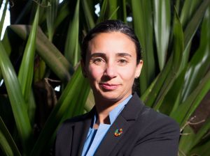 Woman in a suit, wearing and SDG pin with green nature in the background