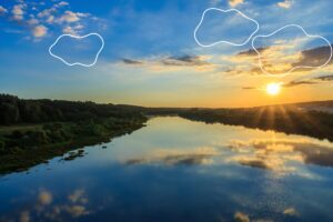 Sunset on the river embankment at summer evening with clouds and trees