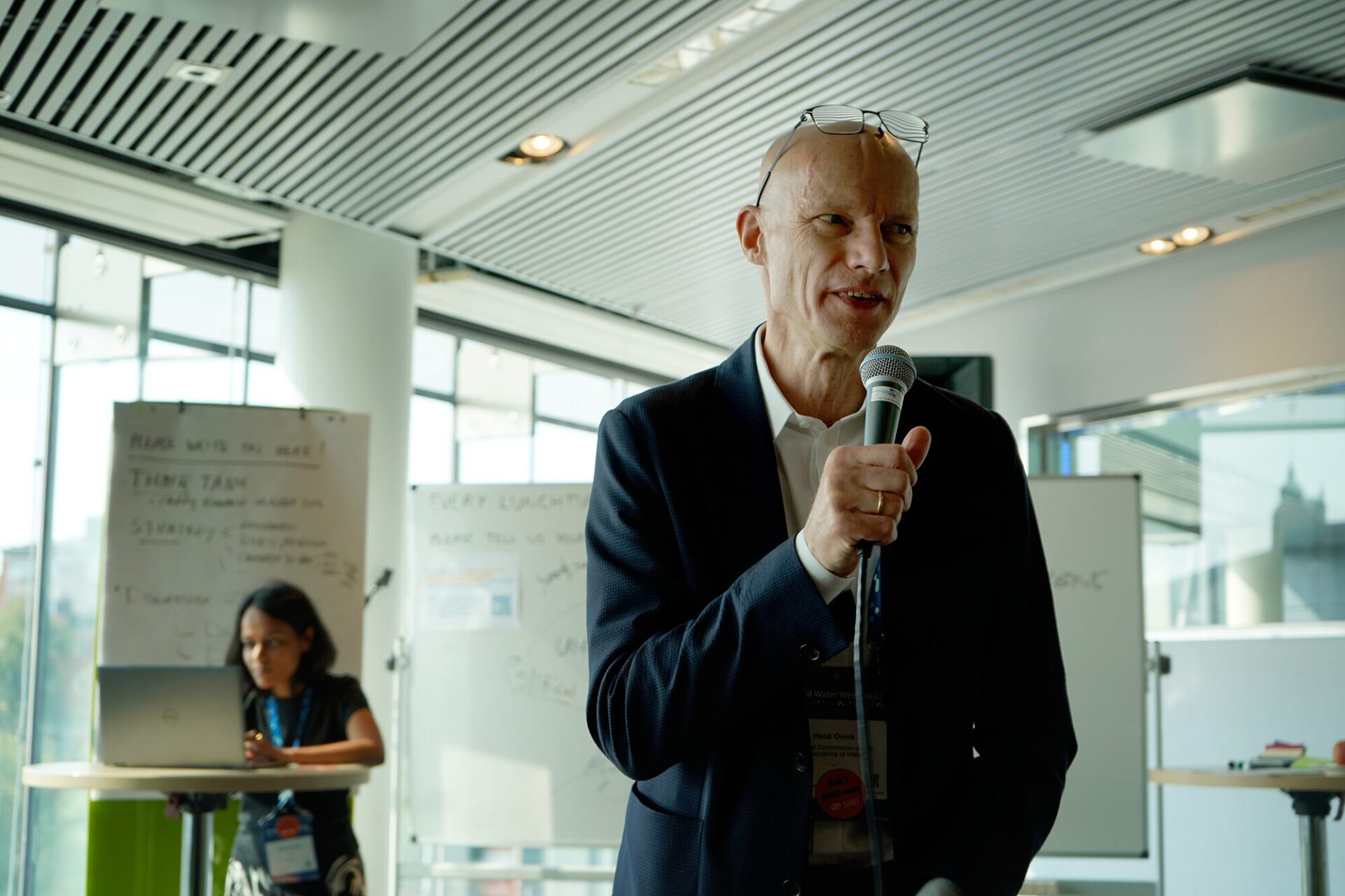 Henk Ovink talking into a microphone. SIWI's Radhika Gupta in the background preparing the interview in the background.